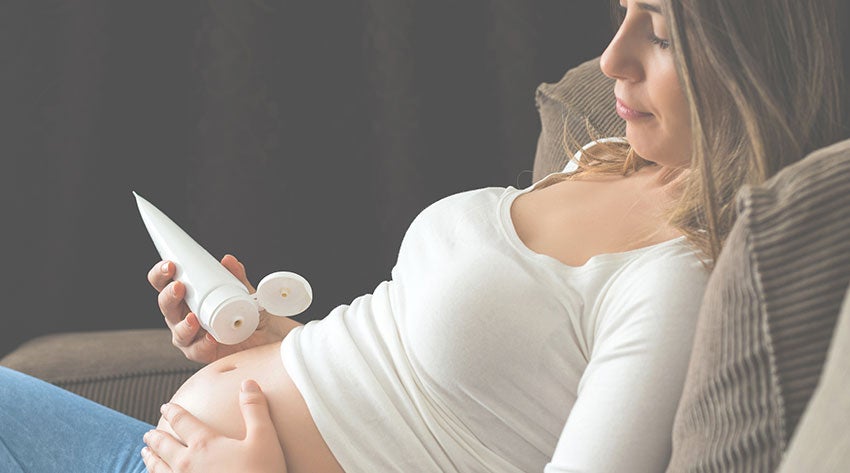 Pregnant mother squeezing cream on to her baby bump