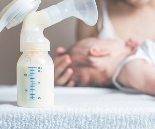 breast milk pump in the foreground and mother comforting her newborn baby in the background
