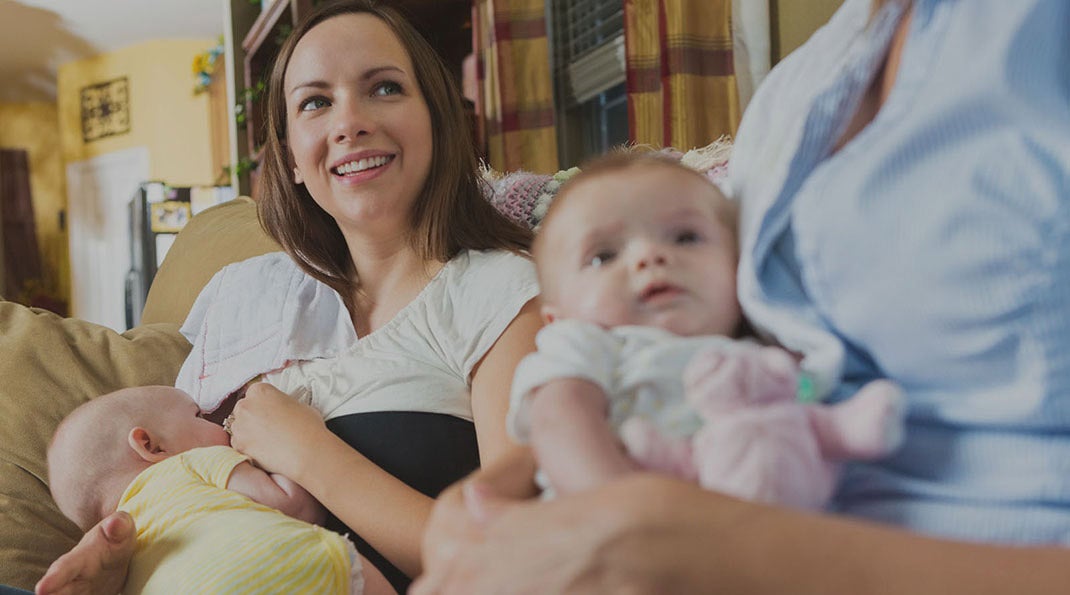 Two mothers holding baby and another mother breastfeeding baby