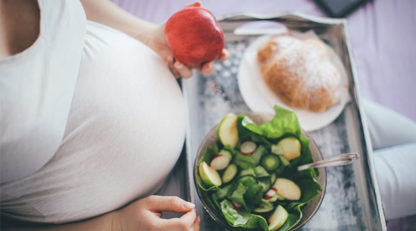 pregnant mother sitting with a food tray on her lap and an apple in her hand