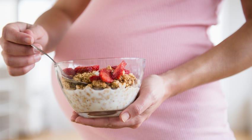 pregnant mother holding a bowl of yoghurt, granola and strawberries