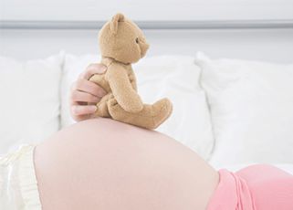 36 weeks pregnant mother holding a teddy bear on her pregnancy bump