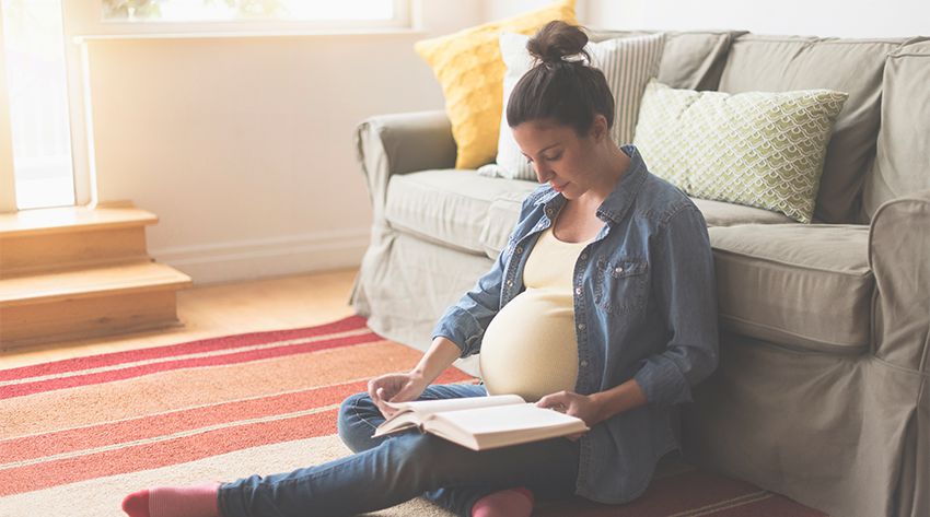 28 weeks pregnant woman reading a book on the floor