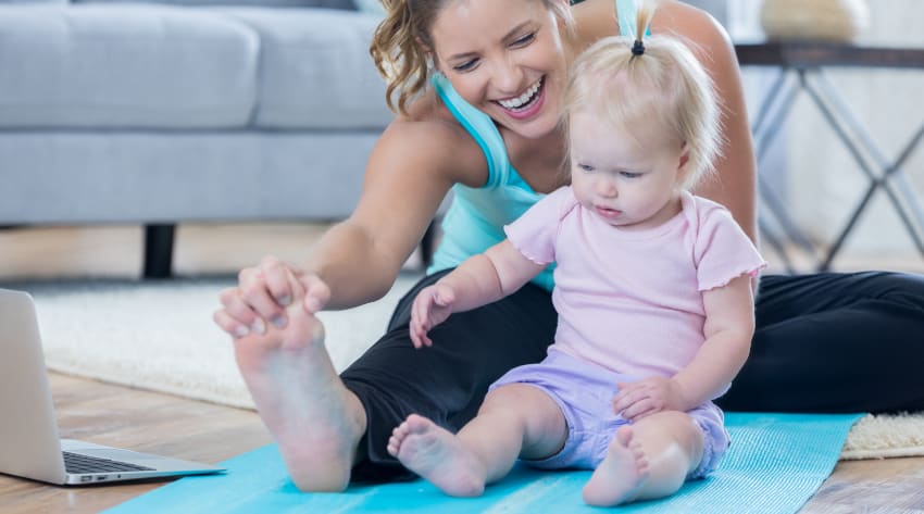 Mother and toddler daughter stretching on a yoga mat