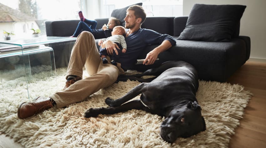 Father with toddler and baby relaxing in front of the TV with their dog