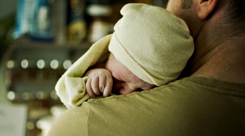 Man cradling newborn baby on his shoulder