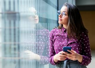 Woman holding a phone, in an office looking out of a window