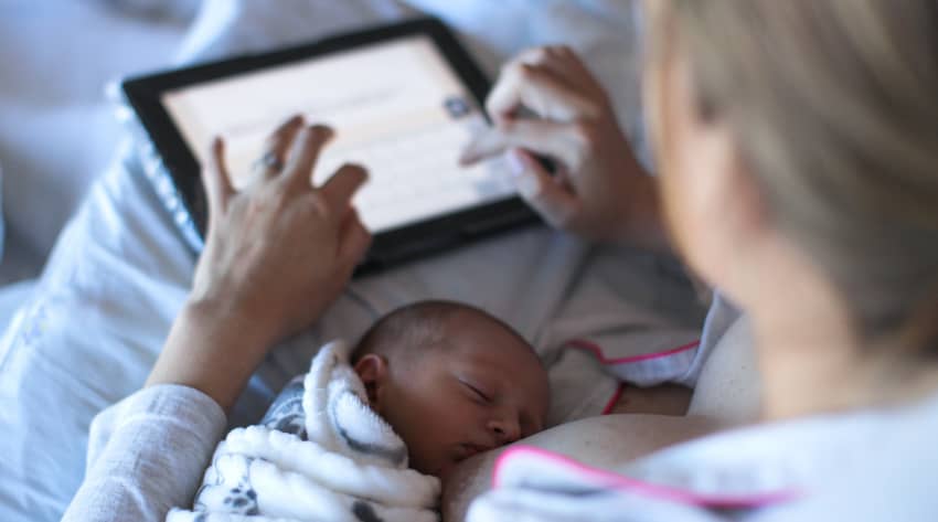 Mother breastfeeding a baby while using a tablet