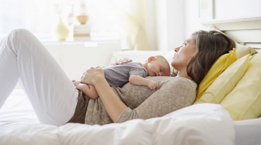 Mother laying in bed looking pensive with a baby on her chest