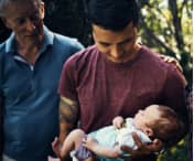 Dad holding newborn surrounded by family
