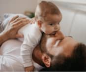 Dad laying down and kissing a baby