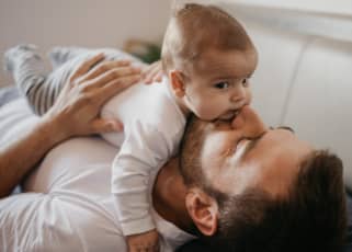 First time dad laying down and hugs newborn across his chest and giving kisses