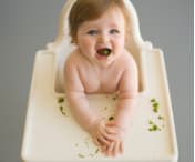 Baby sat on a baby-chair eating broccoli