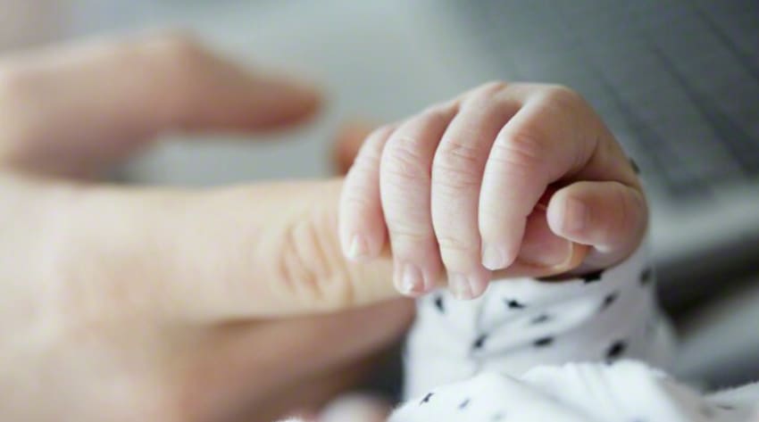 A newborn child holding their parent’s finger