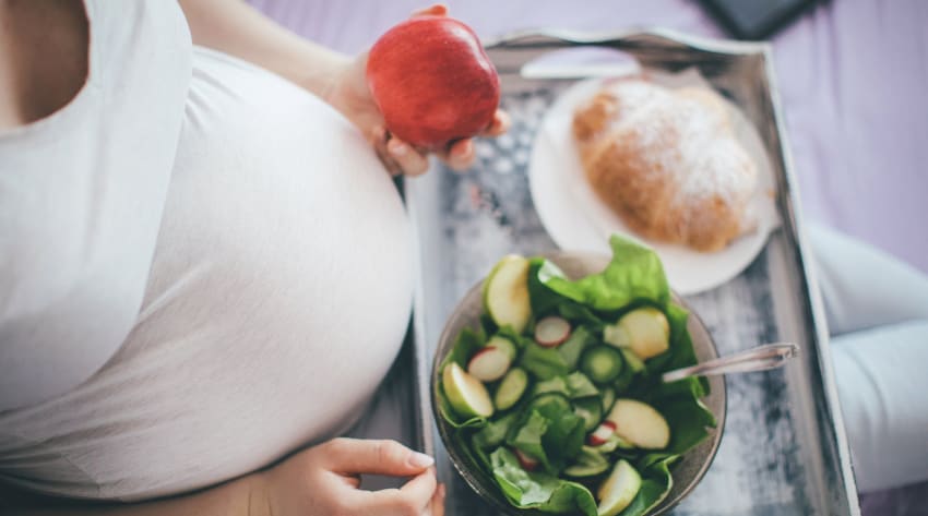 A pregnant woman with a tray of food holding an apple