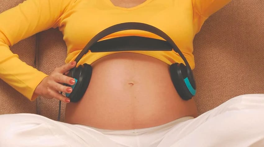 Mother placing headphones over baby bump