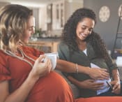 Two pregnant women socialising over a hot beverage.