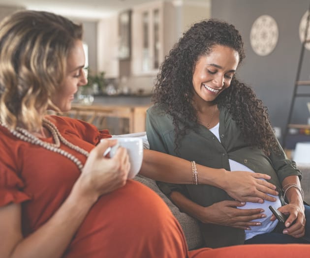 Two pregnant women socialising over a hot beverage.