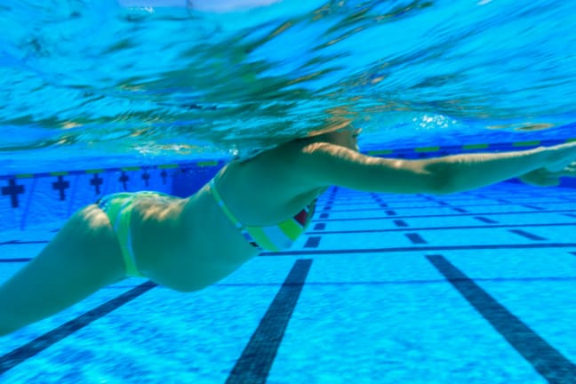 A woman in a bikini that is 24 weeks pregnant swimming in a pool with lanes.