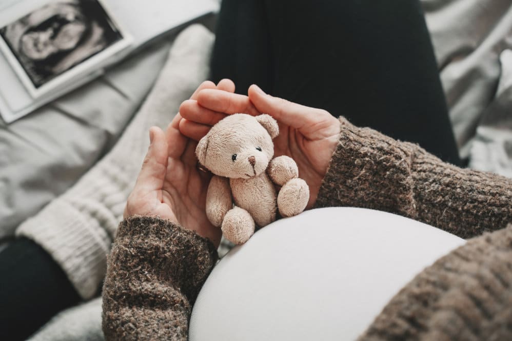 A 36 weeks pregnant woman holding a small toy up to her baby bump