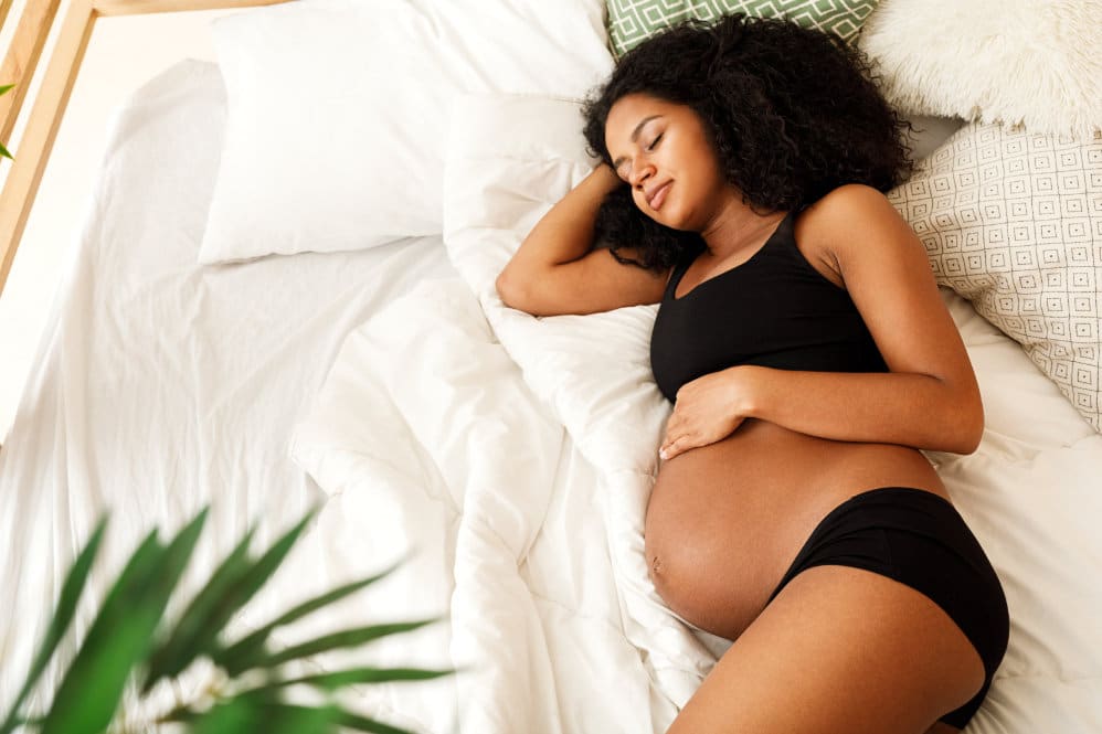 A 37 weeks pregnant woman laying in her bed, while holding her baby bump