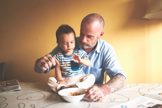 A father feeding his child who is sitting on the table