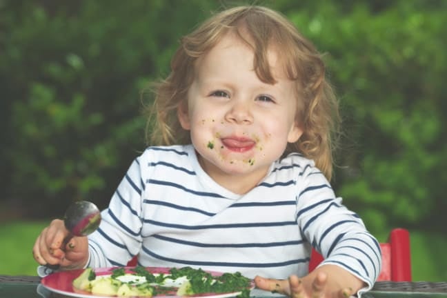 A toddler eating a plate of vegetables
