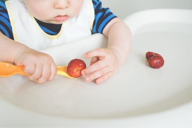 Baby using a spoon to eat fruit during mealtime