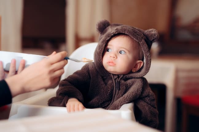 Baby being fed with a spoon while sitting in a high chair