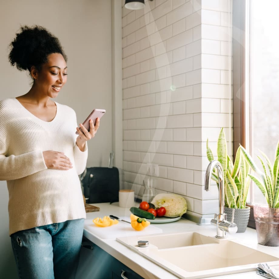 Pregnant woman in a kitchen using a mobile phone