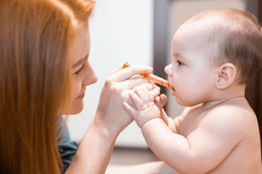 Adult dosing liquid medicine to a baby sitting on a changing mat