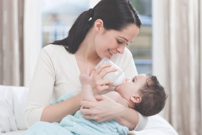 Parent feeds an infant with a bottle of formula milk