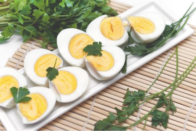 Hard-boiled eggs arranged on a white rectangular platter, garnished with fresh parsley and chives, resting on a bamboo placem