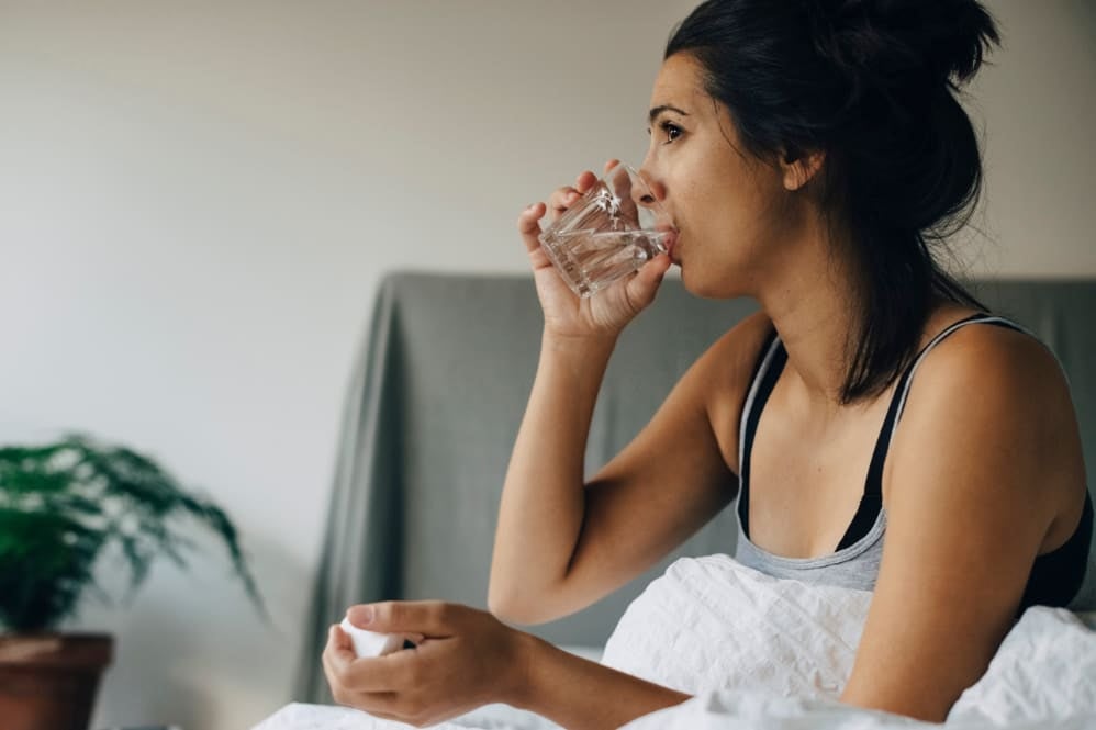Person taking medication and drinking water during early C-section recovery