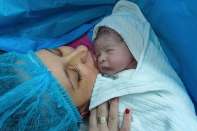 Mother in a surgical cap holding her newborn baby shortly after a c-section birth