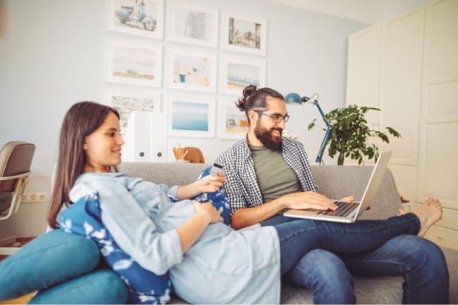 A pregnant woman holding a credit card, sitting beside her partner who is using a laptop