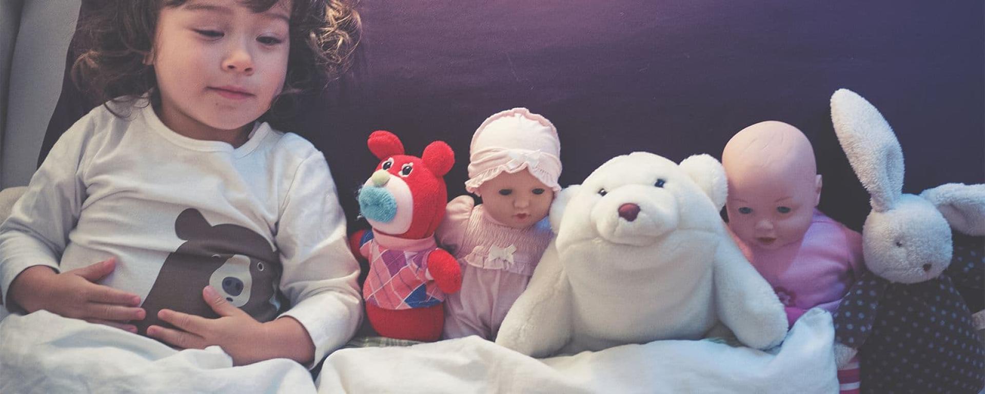 Toddler with toys in bed ready to sleep