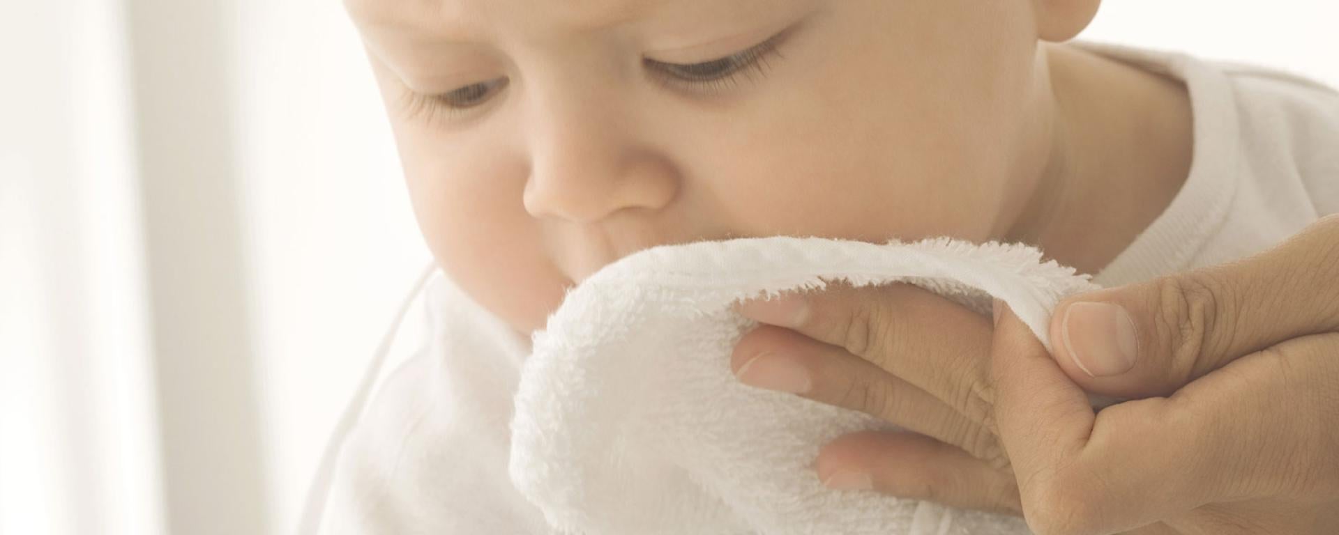 Parent cleaning newborn's face with cotton wool